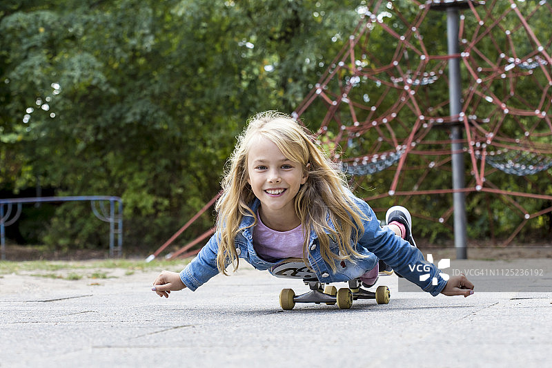 在操场上玩滑板的微笑金发女孩的肖像图片素材