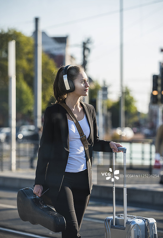 年轻女人戴耳机，手提箱和装着小提琴的盒子在电车站图片素材
