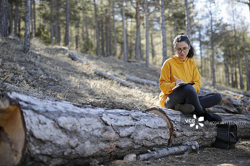 在森林里写作的年轻女子，身穿黄色毛衣图片素材