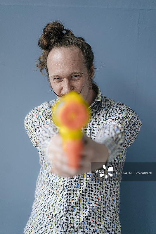 手持水枪的胡子男人肖像，蓝色墙壁图片素材