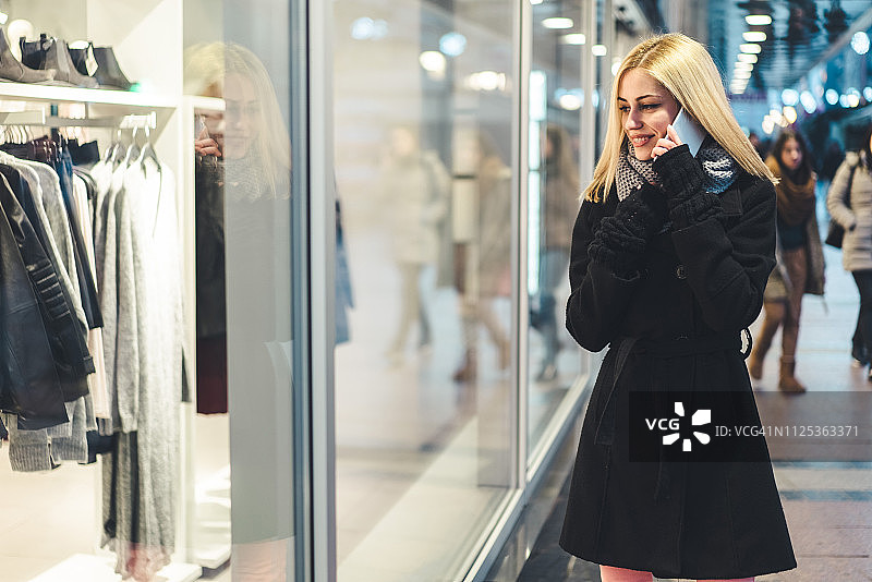 金发女孩在橱窗前看手机图片素材