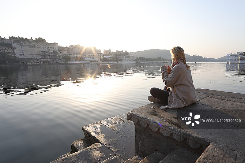 女人日出时在湖边石阶上放松图片素材
