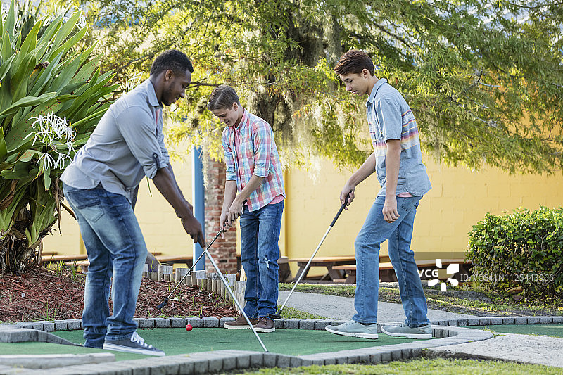 三个多种族青少年男孩在打迷你高尔夫图片素材