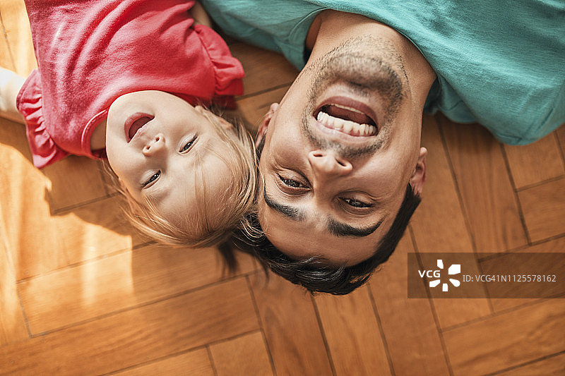 父亲和小女儿躺在家里地板上玩耍的肖像图片素材