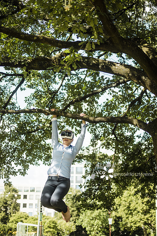 在城市公园里戴VR眼镜、挂在树枝上的女人图片素材