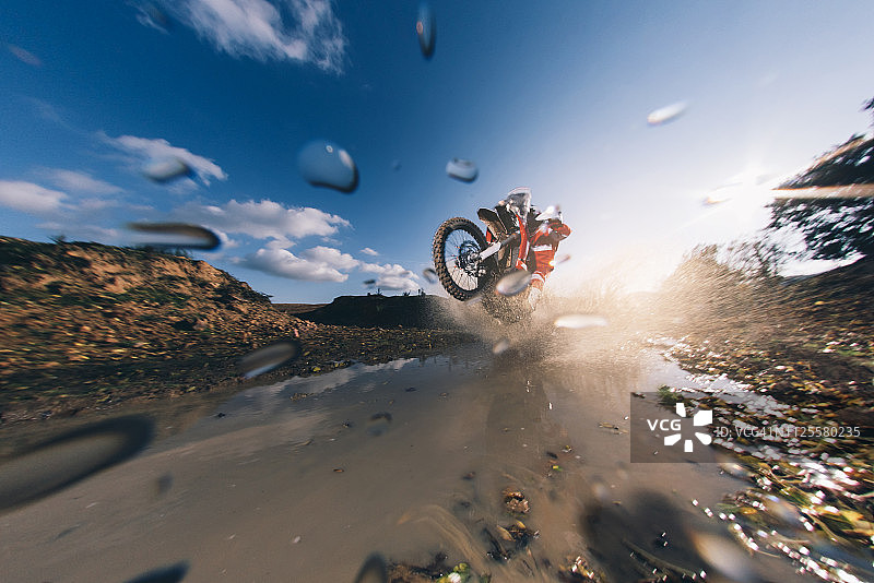摩托车越野赛车手在水中行驶，水花四溅图片素材