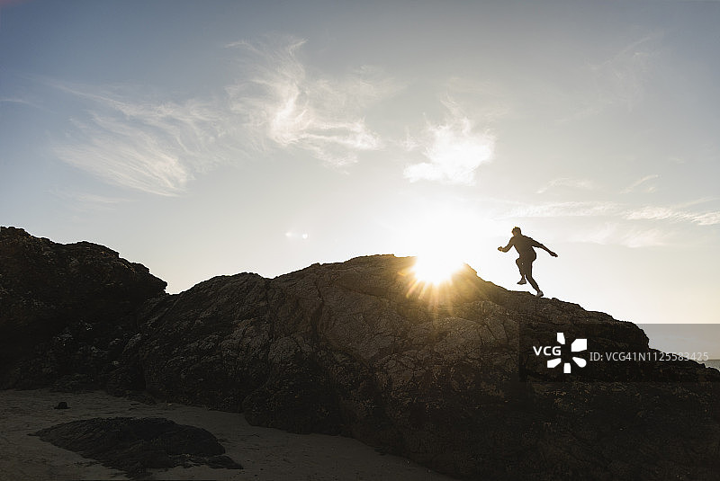 法国布列塔尼：日落时在岩石上奔跑的男子图片素材
