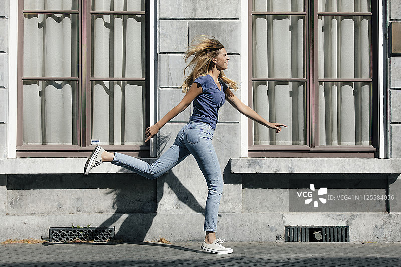 荷兰马斯特里赫特，快乐的金发年轻女人沿着城市建筑奔跑图片素材