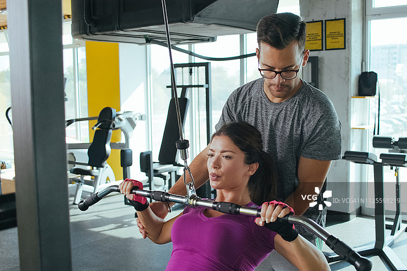 指导员帮助妇女进行滑轮下拉负重练习图片素材