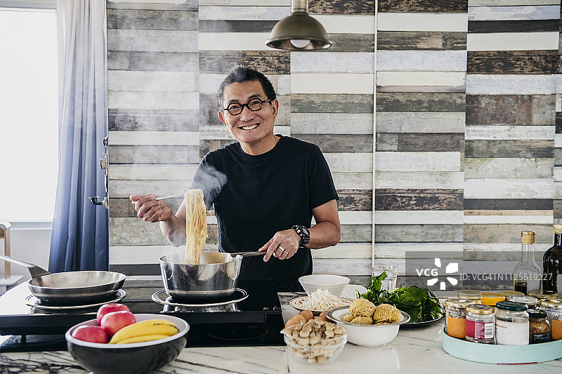 在厨房烹饪意大利面的快乐华人男子图片素材