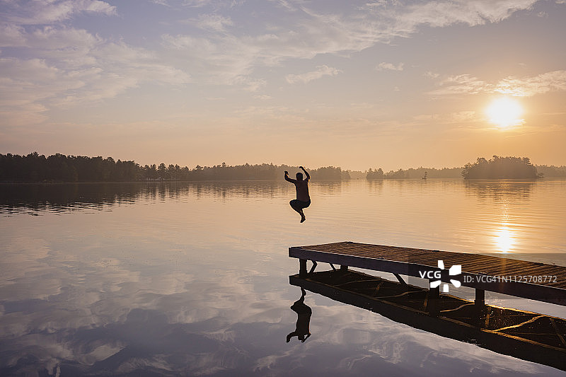 日出时分，男子从码头跳入湖中图片素材