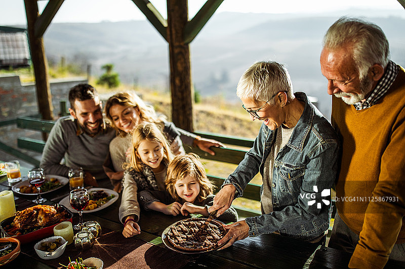 快乐的中年妇女在露台上为家人切甜馅饼。图片素材