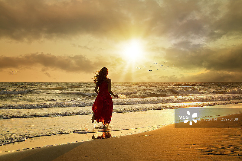 在日落时分海滩上身穿漂亮连衣裙的迷人女性图片素材