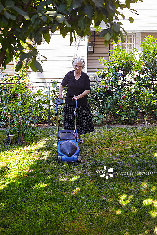 年长的妇女在花园里园艺和用割草机割草图片素材