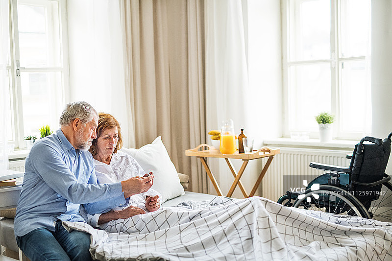 一对年长的夫妇在家中，丈夫照顾他残疾的妻子。图片素材