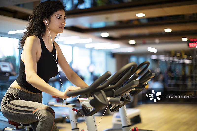 年轻女人在健身房的动感单车上做有氧运动图片素材