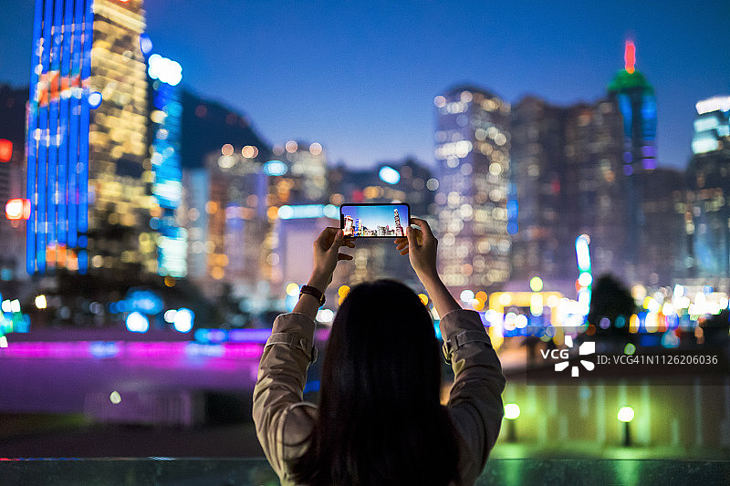 年轻女人用智能手机拍摄香港壮丽夜景图片素材