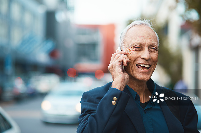 在城市街道上用电话愉快地笑着的成熟商人图片素材