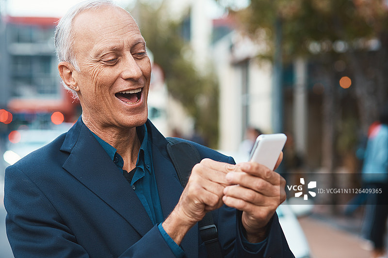 年长的城市商人在手机上笑着看东西图片素材