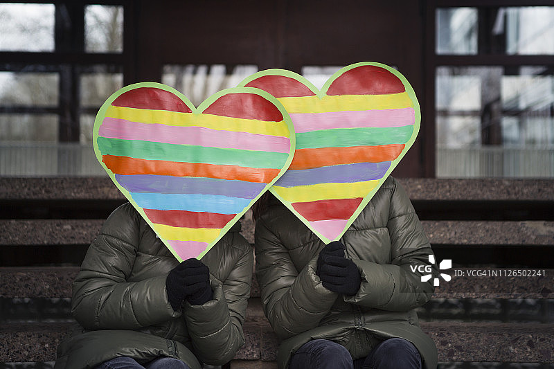 两个孩子拿着彩虹爱心，坐在学校大楼外的台阶上图片素材