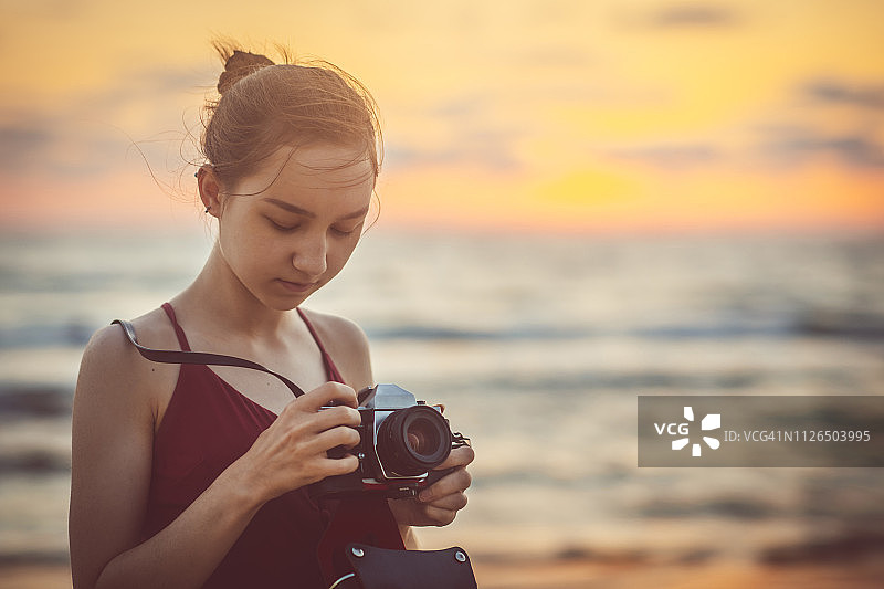 女孩在海边用胶片相机拍照，日落时分图片素材