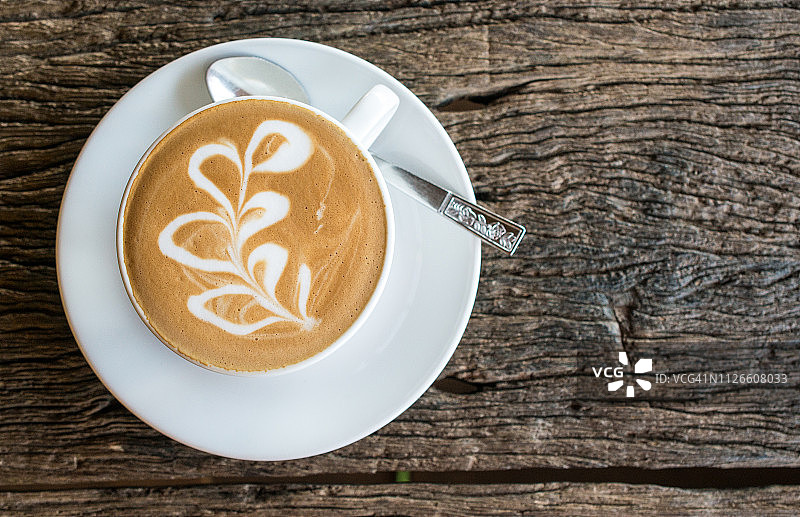一杯带有拉花的热拿铁咖啡，置于木桌上图片素材