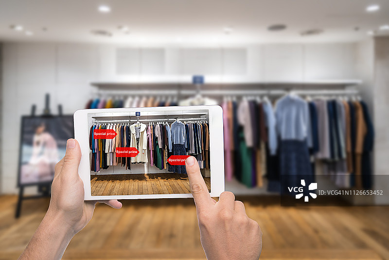 增强现实营销概念：手持数字平板智能手机使用AR应用查看零售时装店商场中的特价图片素材
