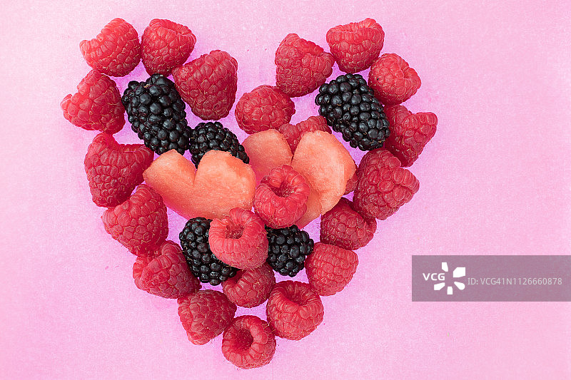 粉色背景上覆盆子、黑莓和西瓜组成的心形特写图片素材