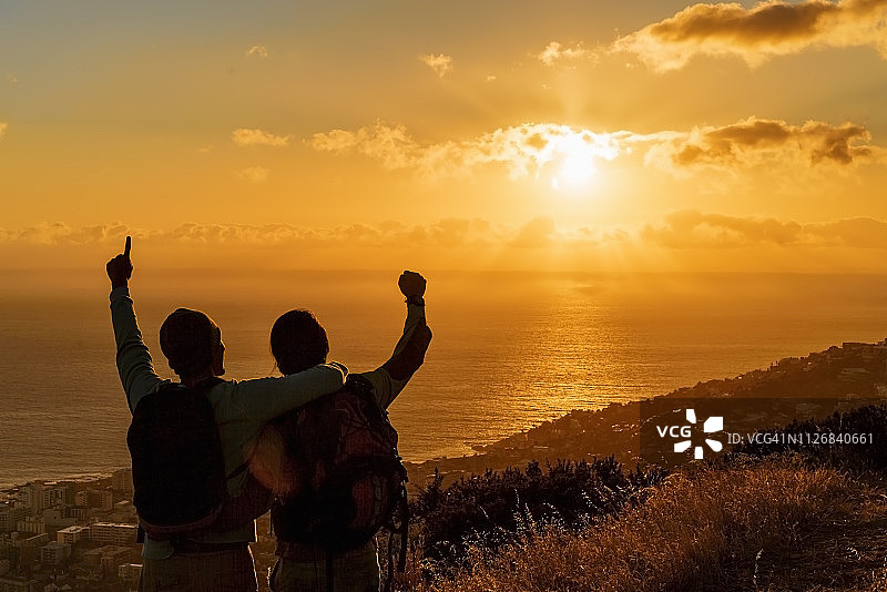 日落时分，兴奋的徒步旅行者在山丘上面朝大海图片素材