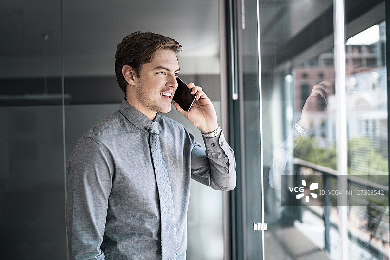 在办公室窗口使用手机的商人图片素材
