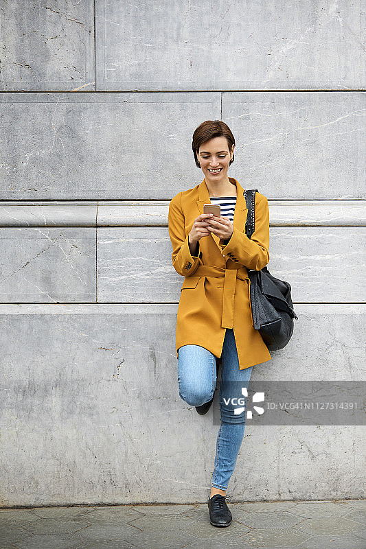 靠墙玩手机的女人图片素材