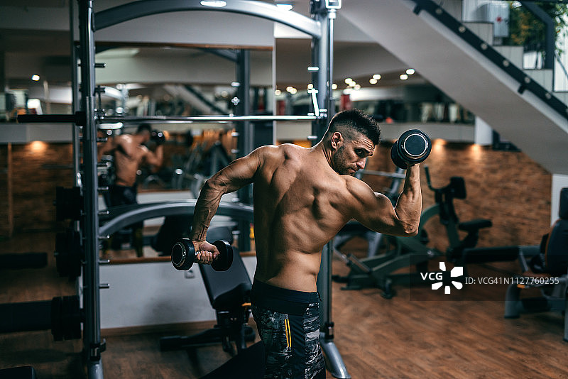 在健身房里用哑铃摆姿势的健壮男人。侧视图。图片素材