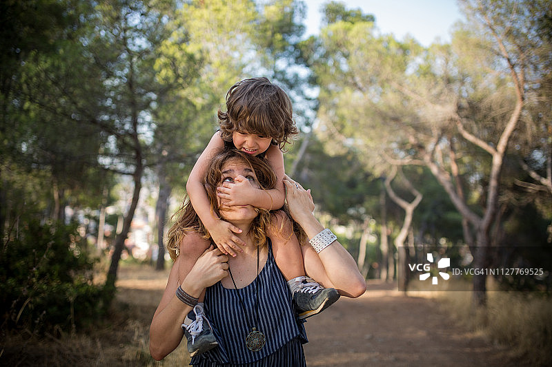 妈妈让蹒跚学步的孩子坐在肩膀上，孩子遮住了她的脸图片素材