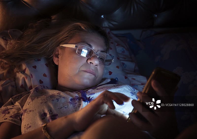 老年妇女躺在床上使用手机（低调）图片素材