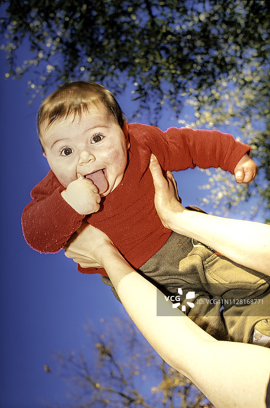 6个月大的快乐微笑的男婴伸出舌头被高高举起图片素材