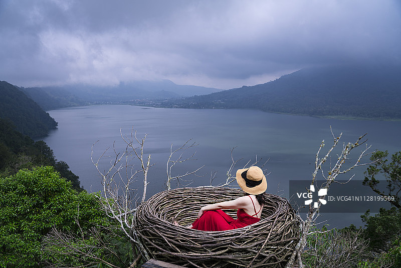 身穿红裙的亚洲女人在人造鸟巢中，背景是美丽的自然风光图片素材