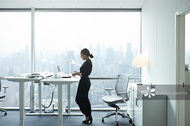 在办公室用电脑工作的女商人，可欣赏美丽的天际线图片素材