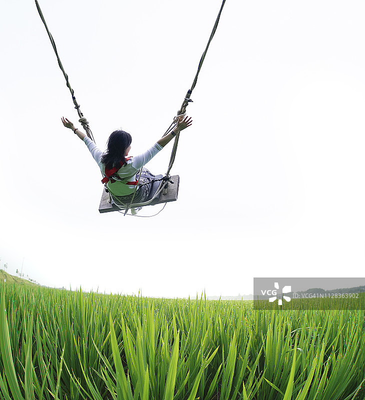 阳光明媚的日子里，年轻女人在草地上荡秋千图片素材