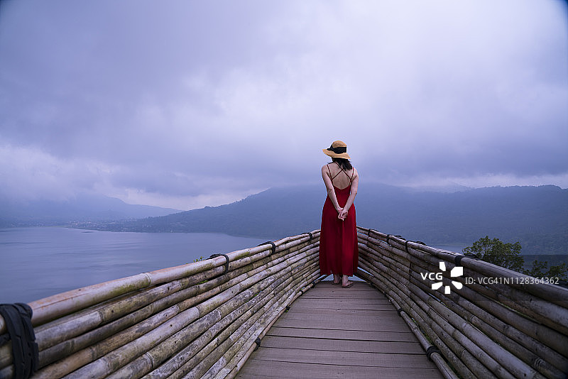 一位身穿红色裙子的亚洲女性眺望湖泊和山脉图片素材