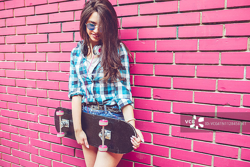女孩靠在有滑板的粉色砖墙旁图片素材