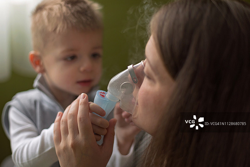 母亲帮助儿子使用雾化器进行吸入治疗图片素材