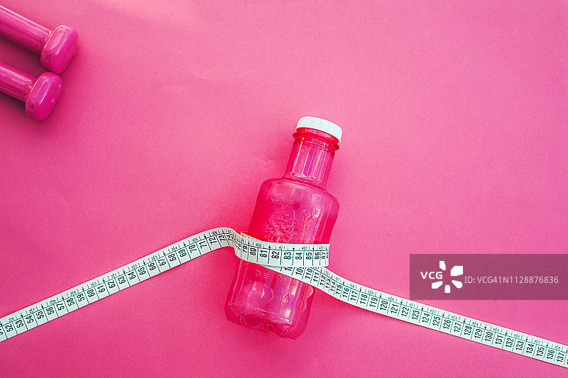 卷尺和水瓶，运动与饮食概念（粉色背景）图片素材