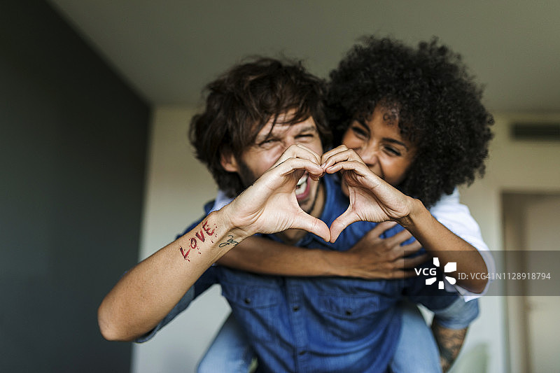 快乐的男人在家背着女朋友，用手比心图片素材