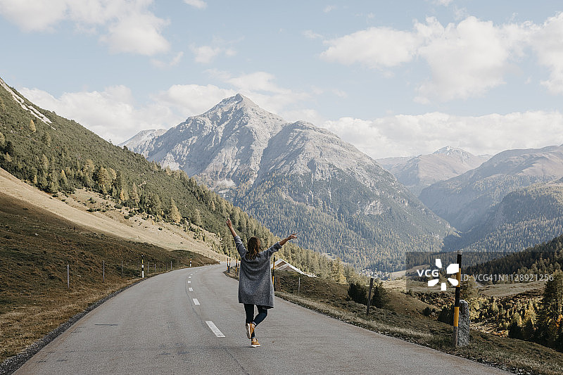 瑞士恩嘎丁：在山路上举起双臂的快乐女人背影图片素材