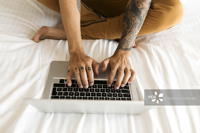 特写：有纹身的男人在床上使用笔记本电脑图片素材