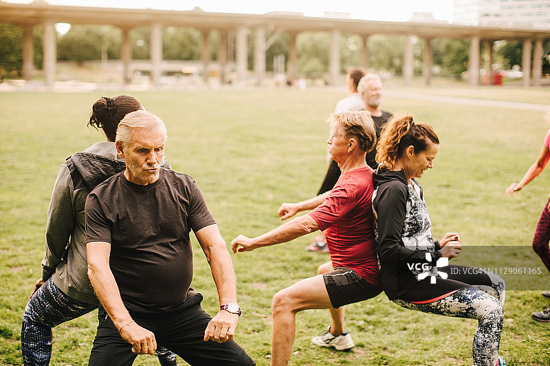 不同种族的朋友在公园背靠背练习深蹲图片素材