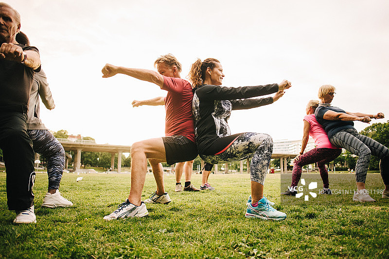 在公园里练习背靠背深蹲的年长运动朋友图片素材