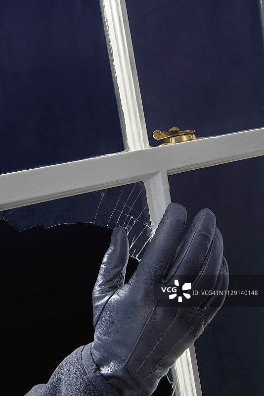 一只戴着手套的手穿过破窗玻璃解锁窗户图片素材