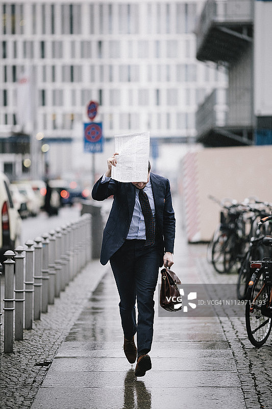 商人用报纸从雨中跑开图片素材
