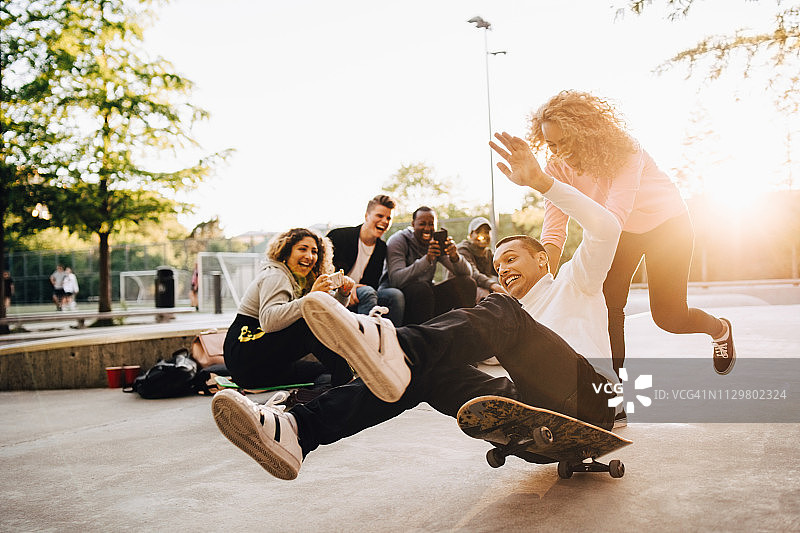 朋友们在公园拍摄男子从滑板上摔下来图片素材
